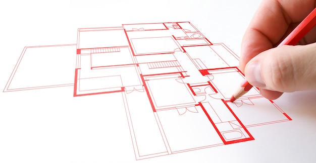 A person drawing a house plan drawing with red pencil paper.